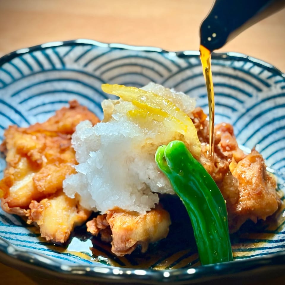 Japanese fried chicken topped with grated daikon, lemon, and green pepper, drizzled with sauce in a blue patterned bowl.