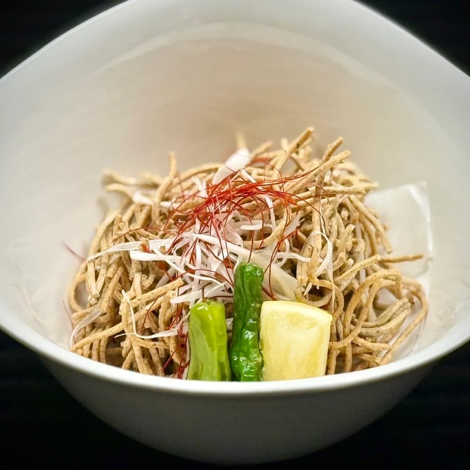 Bowl of crispy shredded noodles garnished with onions, red chili threads, green peppers, and a lemon wedge.
